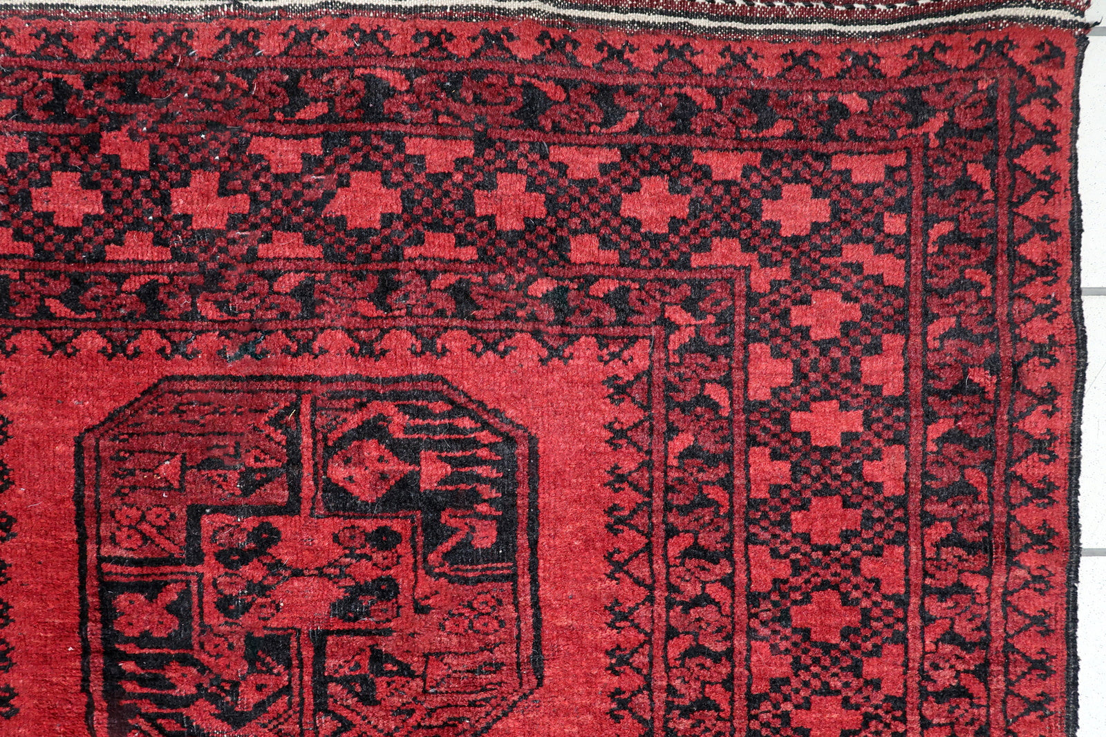 Close-up of intricate geometric detailing inside a midnight black elephant foot gul on a vintage Afghan tribal carpet