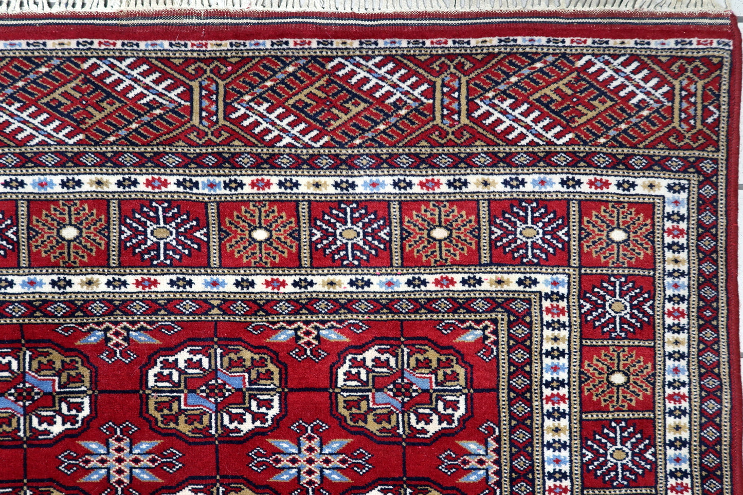 Close-up of intricate ivory, navy blue and copper-toned detailing inside traditional Bukhara guls on a Central Asian carpet