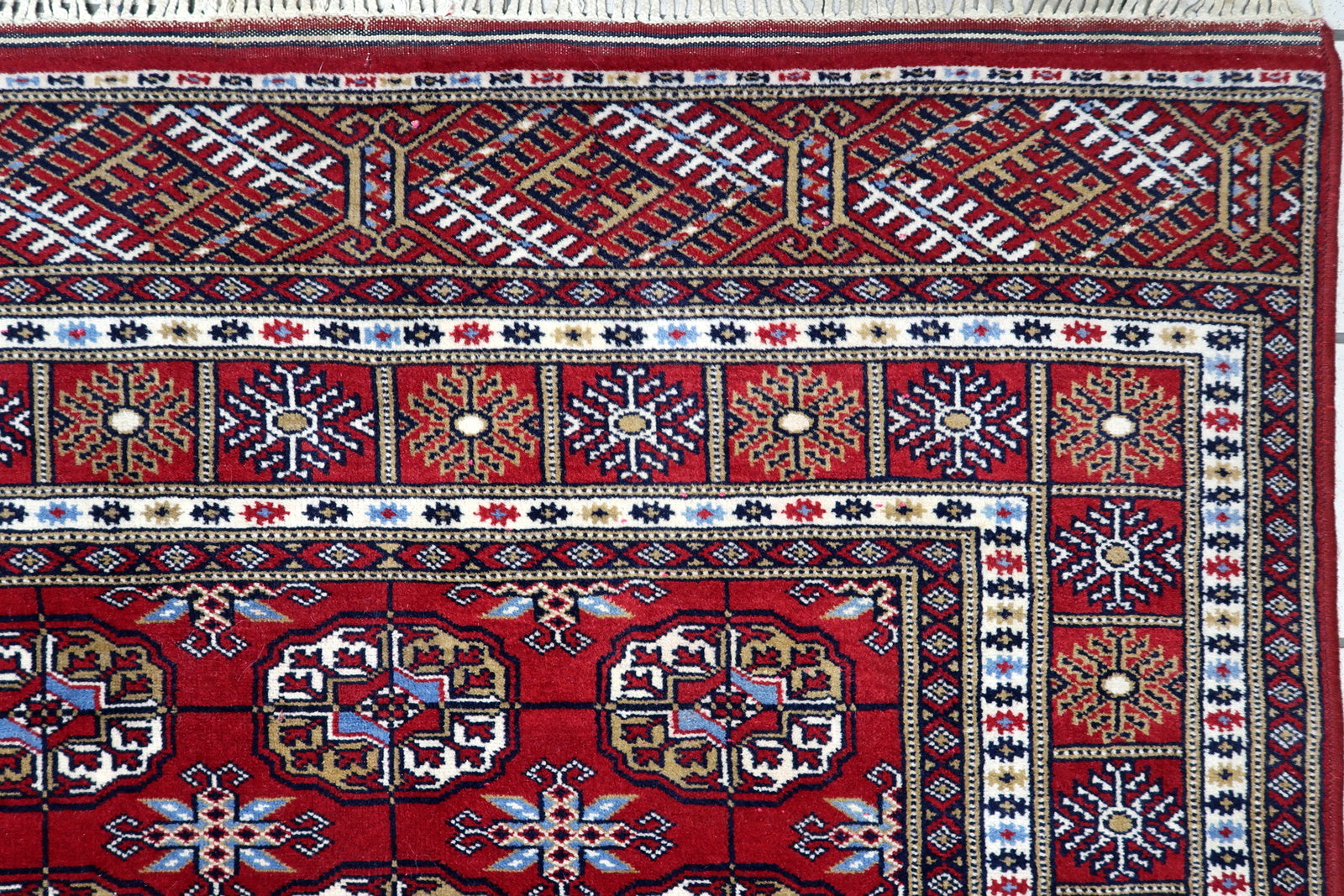 Close-up of intricate ivory, navy blue and copper-toned detailing inside traditional Bukhara guls on a Central Asian carpet