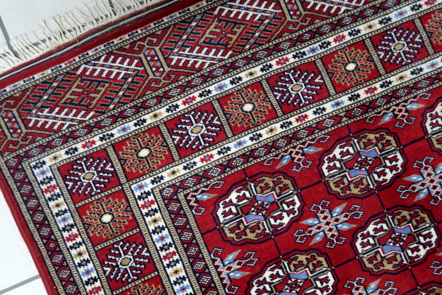 Full view of a vintage tribal rug featuring dense geometric pattern with multiple guard bands and sunburst borders