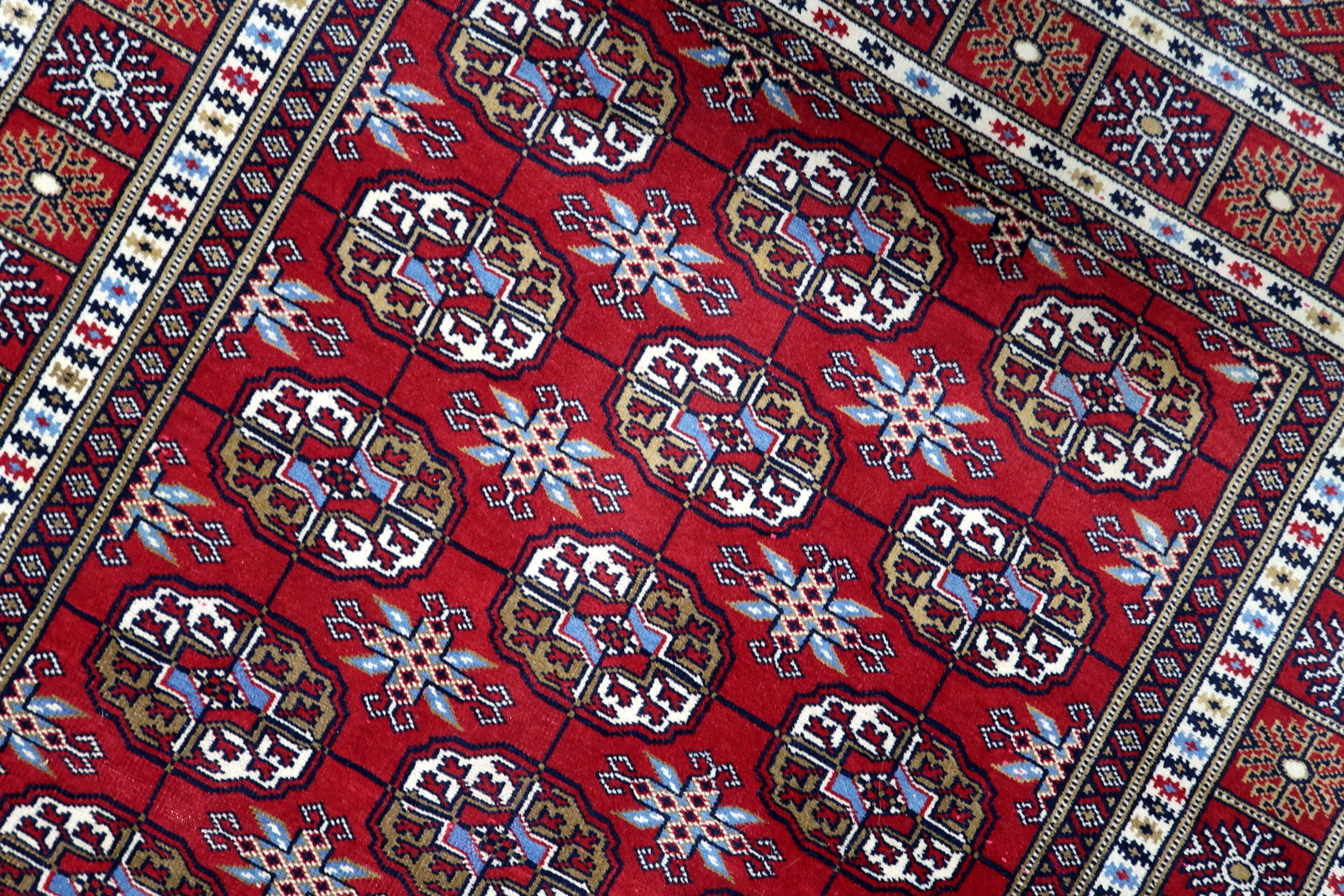 Detailed border showing delicate sunburst and geometric tile motifs framing the crimson field with architectural elegance