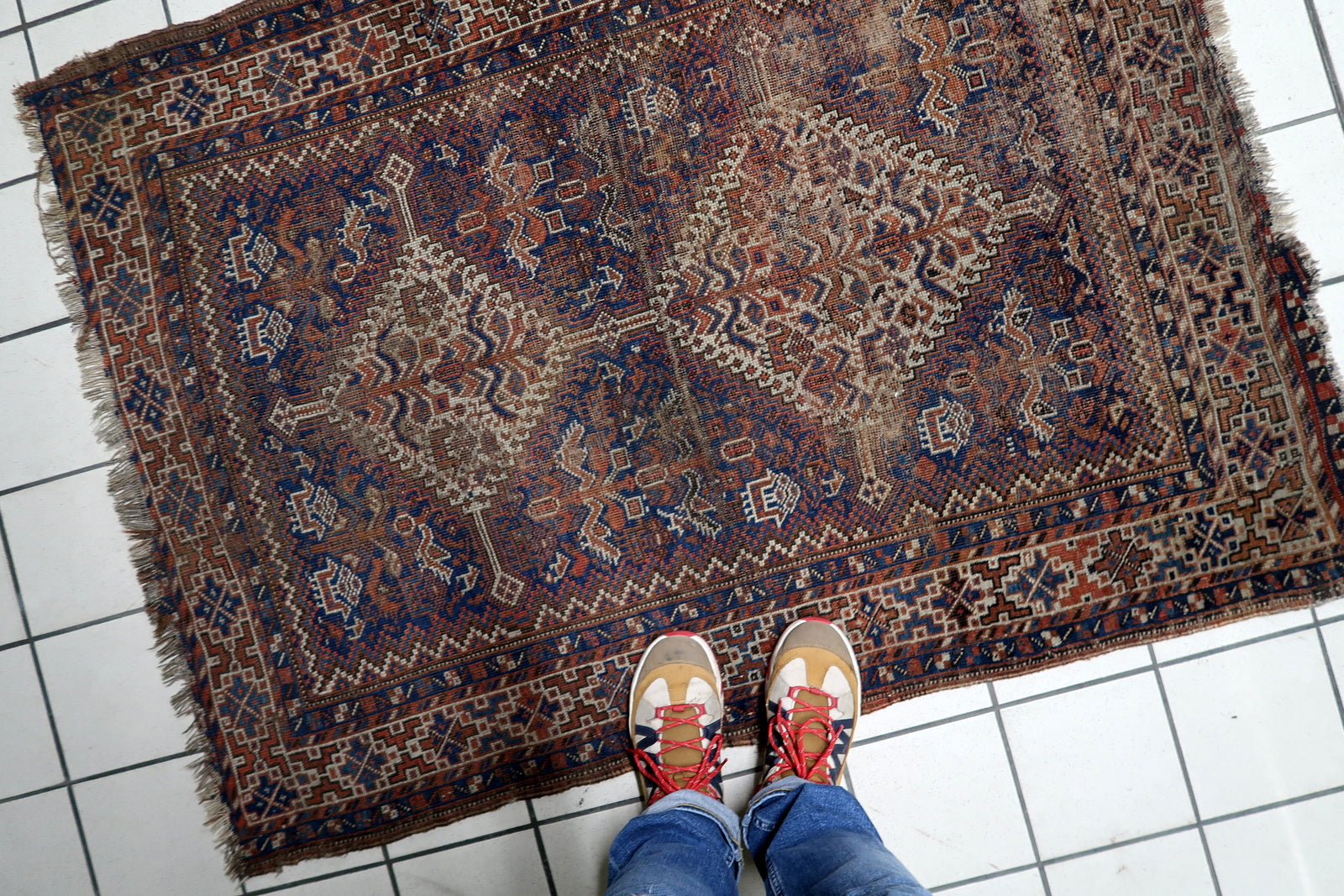 Hand-knotted wool rug in worn distressed condition featuring authentic low pile and structural integrity intact