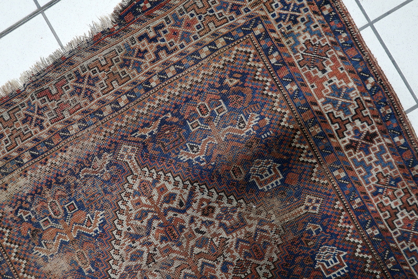 Full view of a 19th century tribal rug featuring series of diamond medallions arranged along the central axis