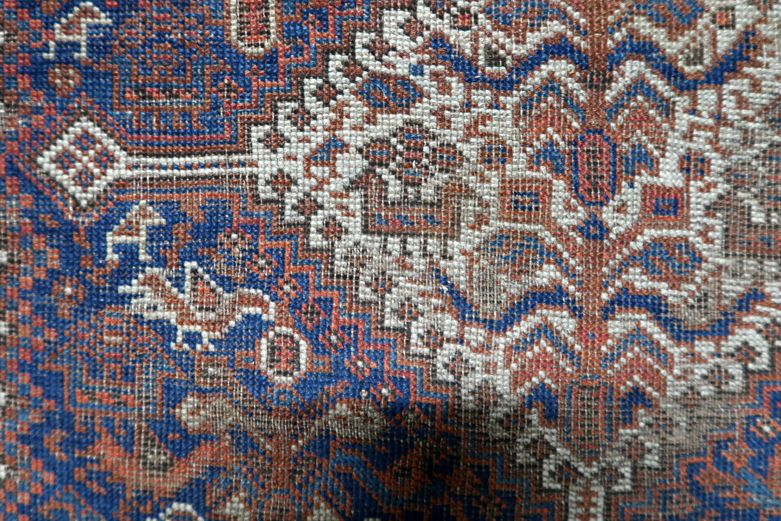 Earthy brown, red, blue and cream antique Persian rug with repeating diamond medallions and expressive tribal geometry