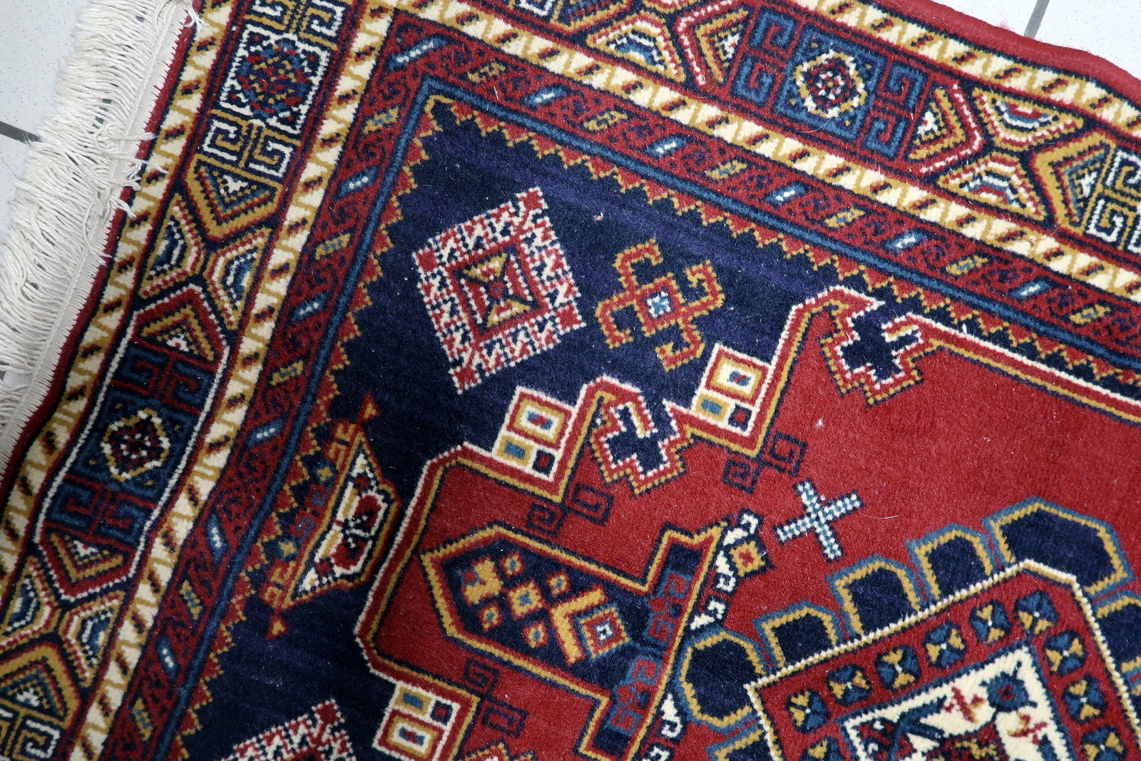 Close-up of angular geometric motifs and rhythmic tribal patterns surrounding the central medallion on a mid-century carpet