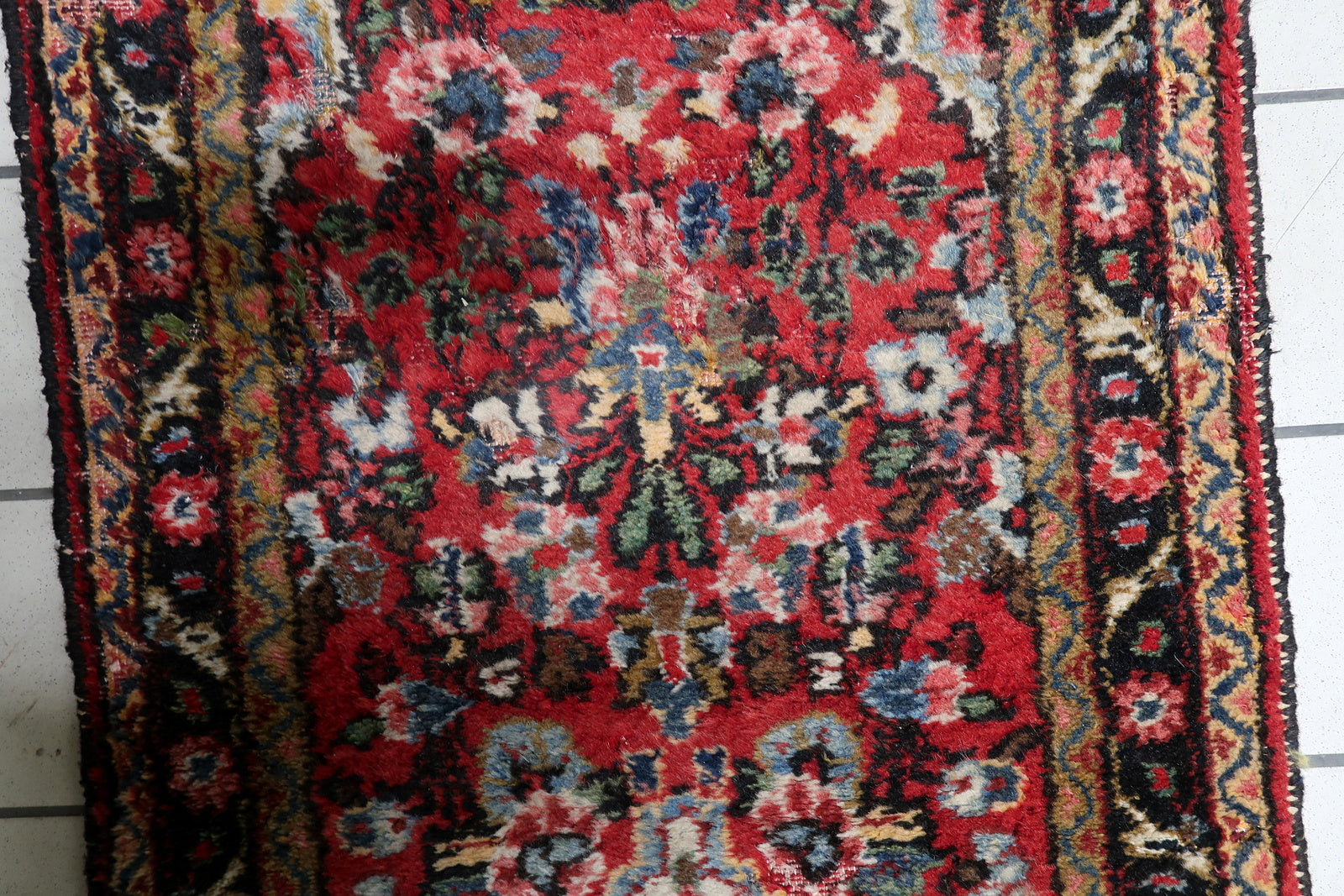 Close-up of time-softened geometric and floral motifs in red, dark blue and ivory on a hand-knotted Persian runner