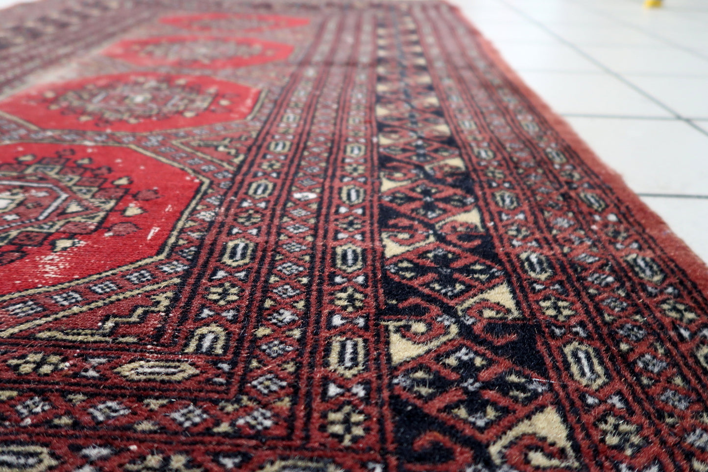 Warm red field with dark brown, black and ivory accents on a distressed Uzbek Bukhara rug with authentic patina