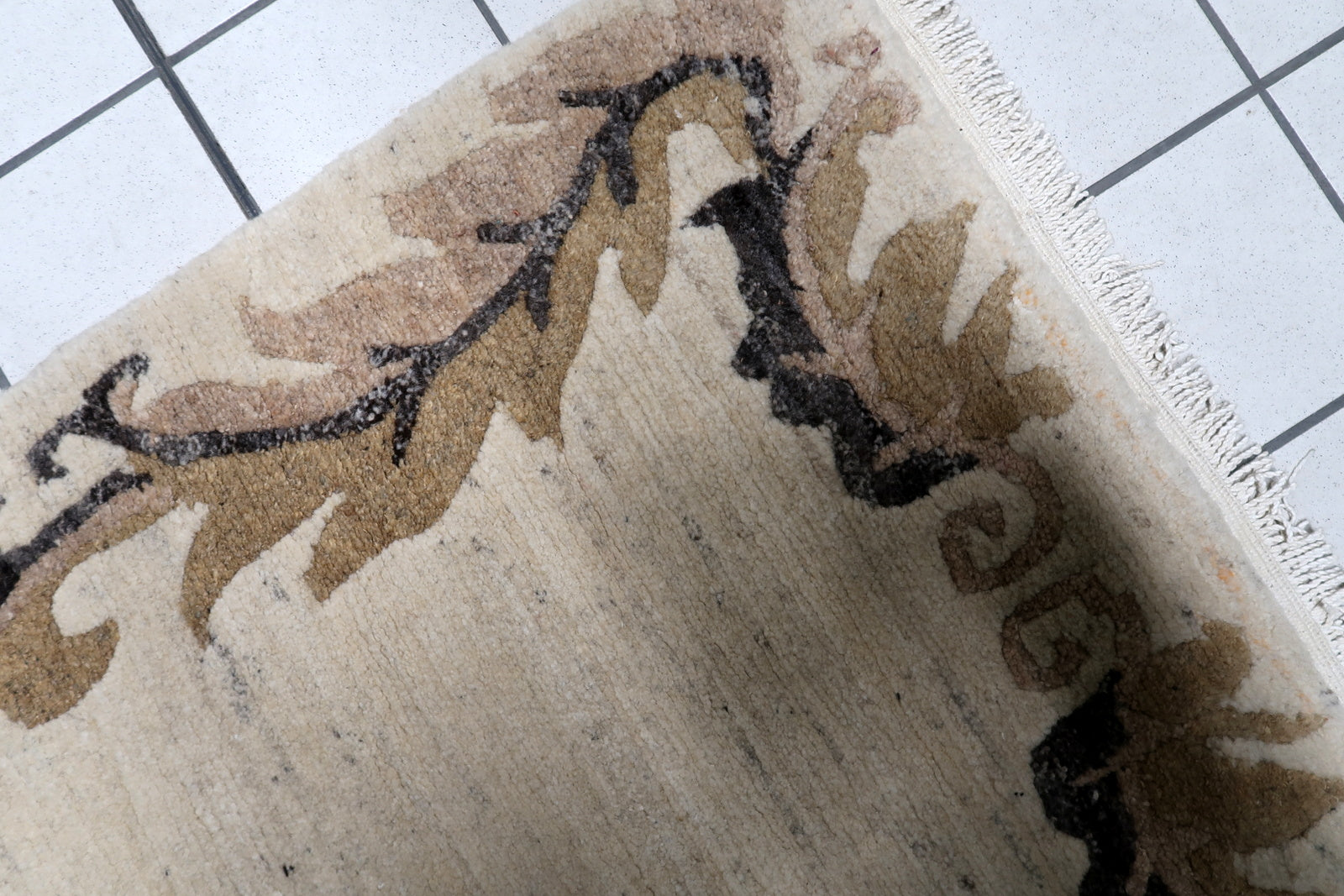 Close-up view of a vintage Tibetan rug's border, showing detailed stylized leaf patterns in warm brown and charcoal on a beige background.

