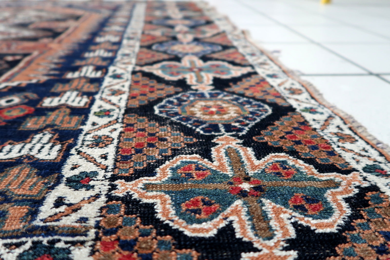 Vintage Persian rug featuring a striking all-over pattern with diamond medallions and geometric florals in classic tribal colors of red, navy, and rust.

