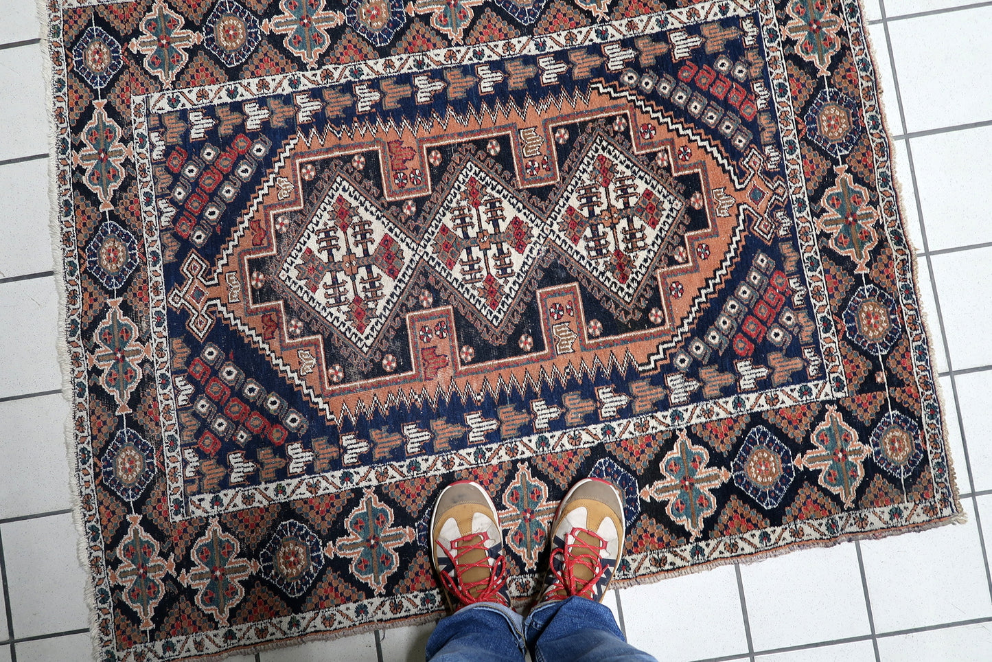 Close-up detail of the intricate geometric patterns and rich color palette—deep navy, rust, and ivory—on a hand-knotted Persian tribal rug.

