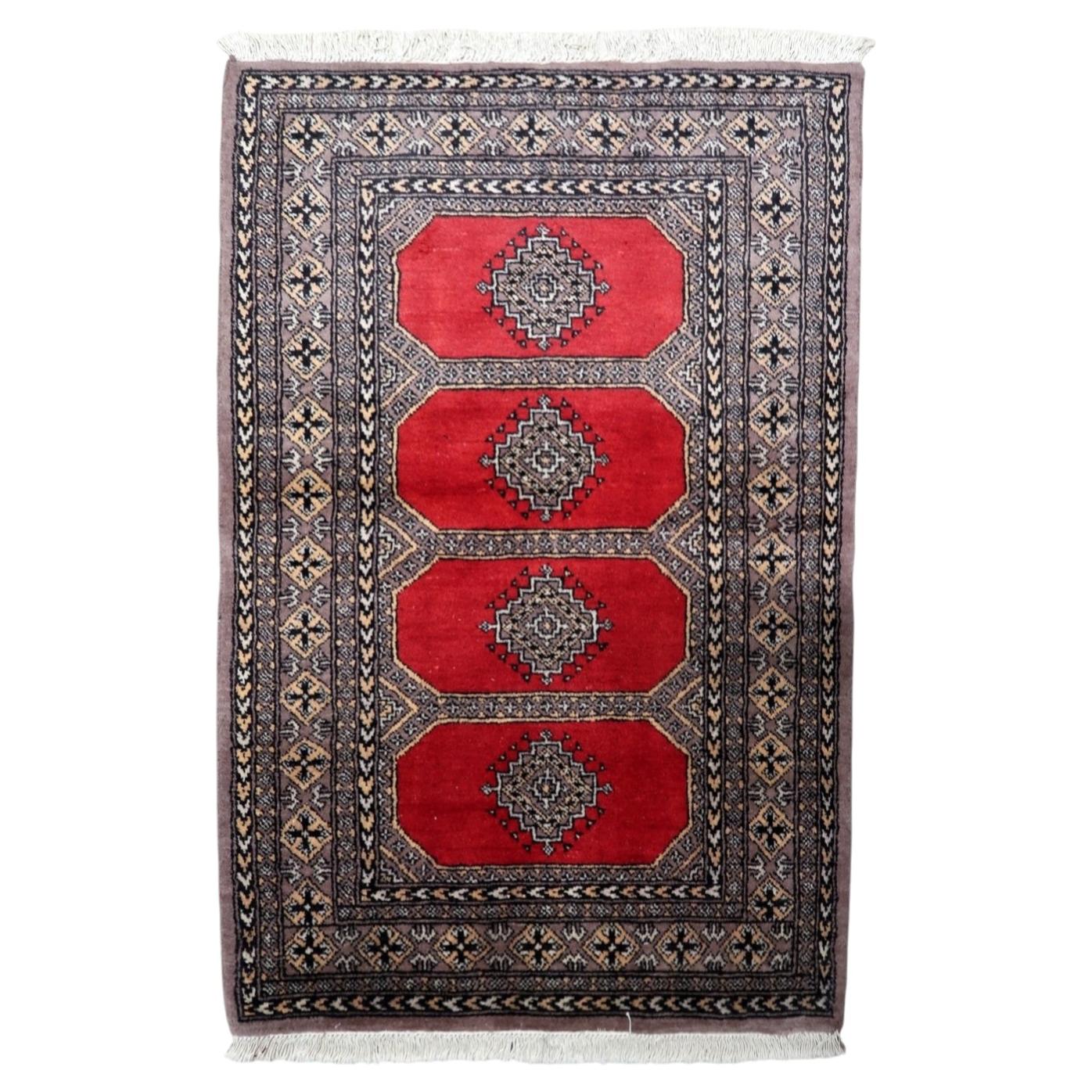 Vintage Uzbek Bukhara rug from the 1960s, hand-knotted wool, featuring four bold octagonal guls on a rich red field with geometric borders.

