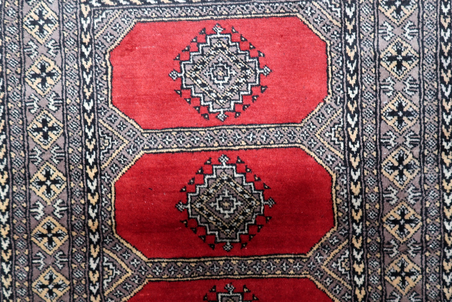 Close-up of an antique-style Uzbek Bukhara rug, highlighting the detailed geometric motifs within a traditional octagonal gul.

