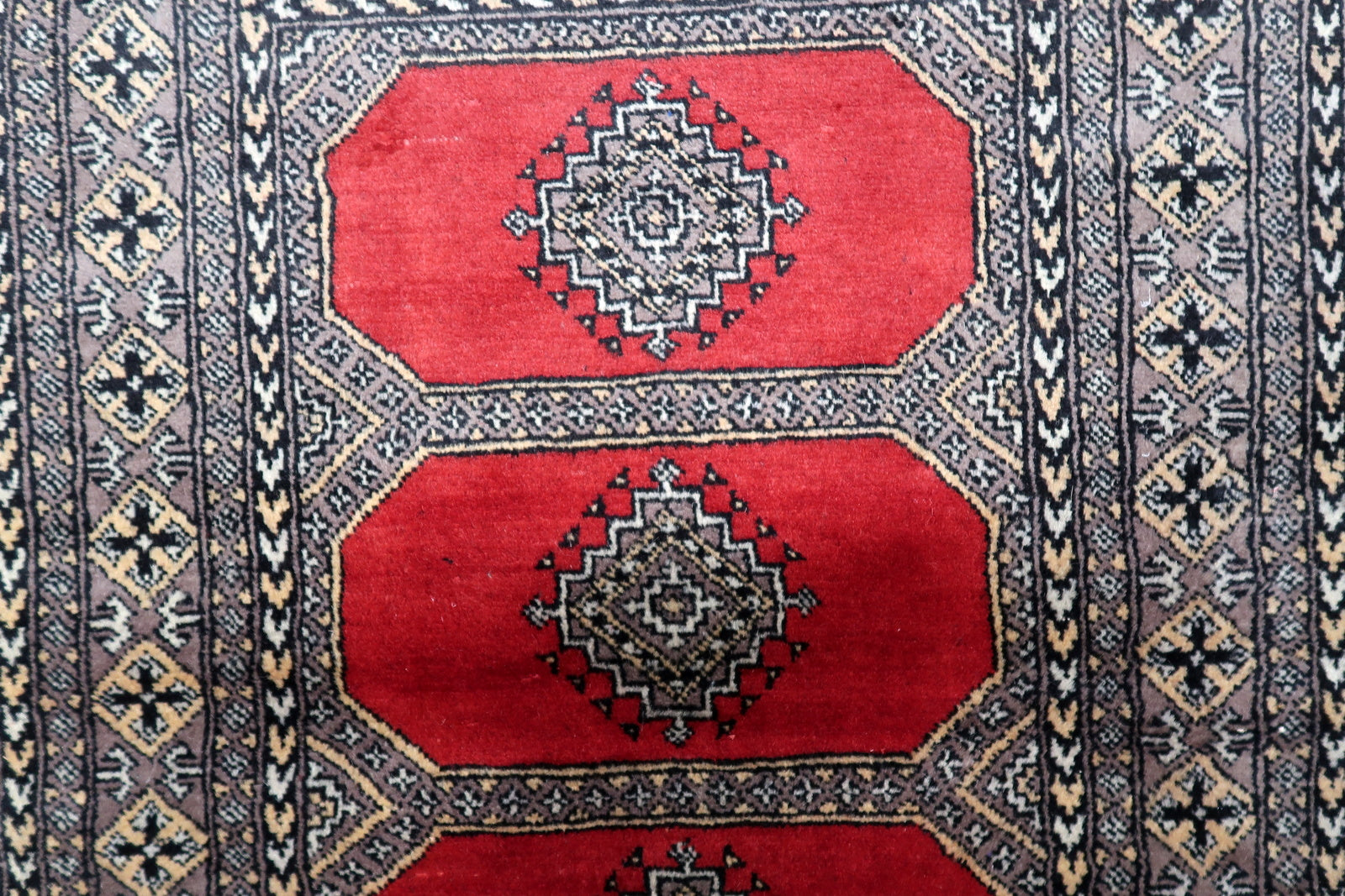 Close-up of an antique-style Uzbek Bukhara rug, highlighting the detailed geometric motifs within a traditional octagonal gul.

