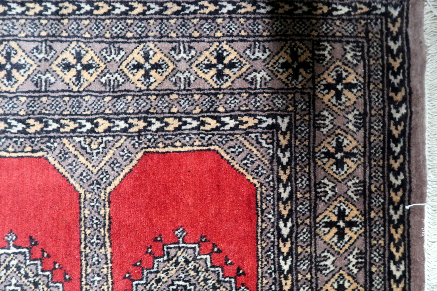 Vintage Bukhara rug with four prominent octagonal guls (elephant's foot motifs) arranged in a rhythmic pattern on a deep red ground.

