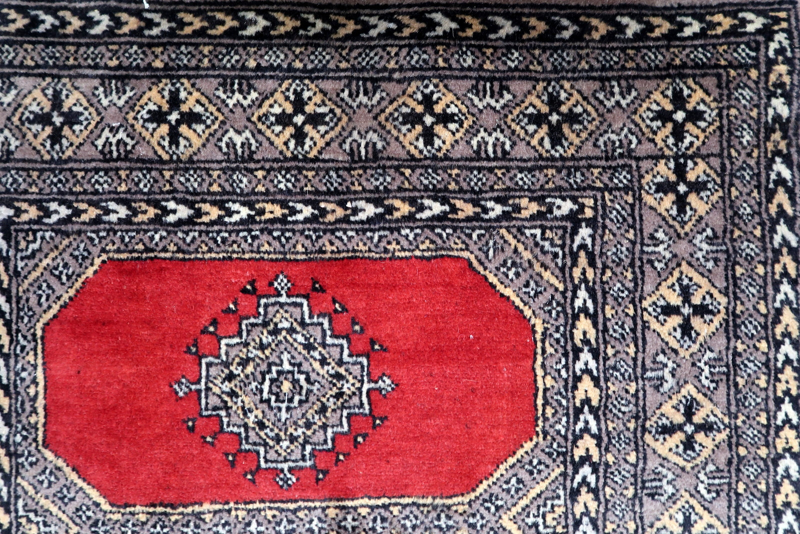 Geometric tribal borders in black, ivory, and beige frame the red field of this 1960s Uzbek Bukhara hand-knotted rug.

