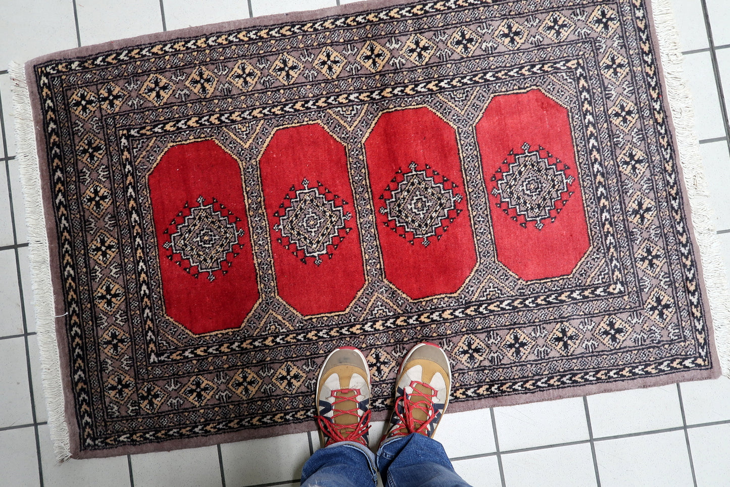 Close-up detail of the intricate geometric patterns within a Bukhara gul, set against the rug's rich red wool background.

