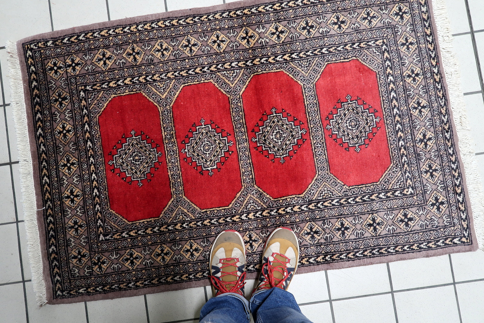 Close-up detail of the intricate geometric patterns within a Bukhara gul, set against the rug's rich red wool background.


