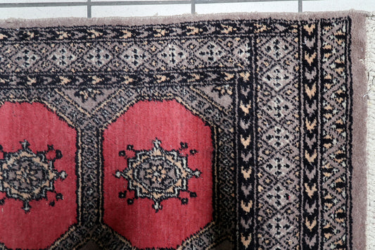 Narrow vintage tribal runner from Uzbekistan with red field and geometric borders on floor

