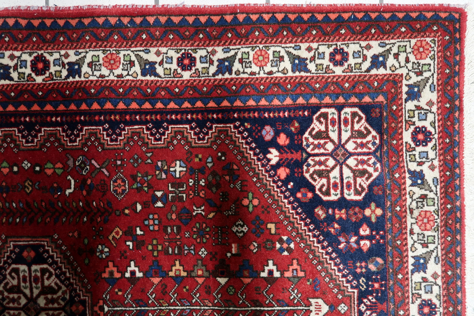 Vintage tribal rug from southern Persia with deep red field and navy borders on floor

