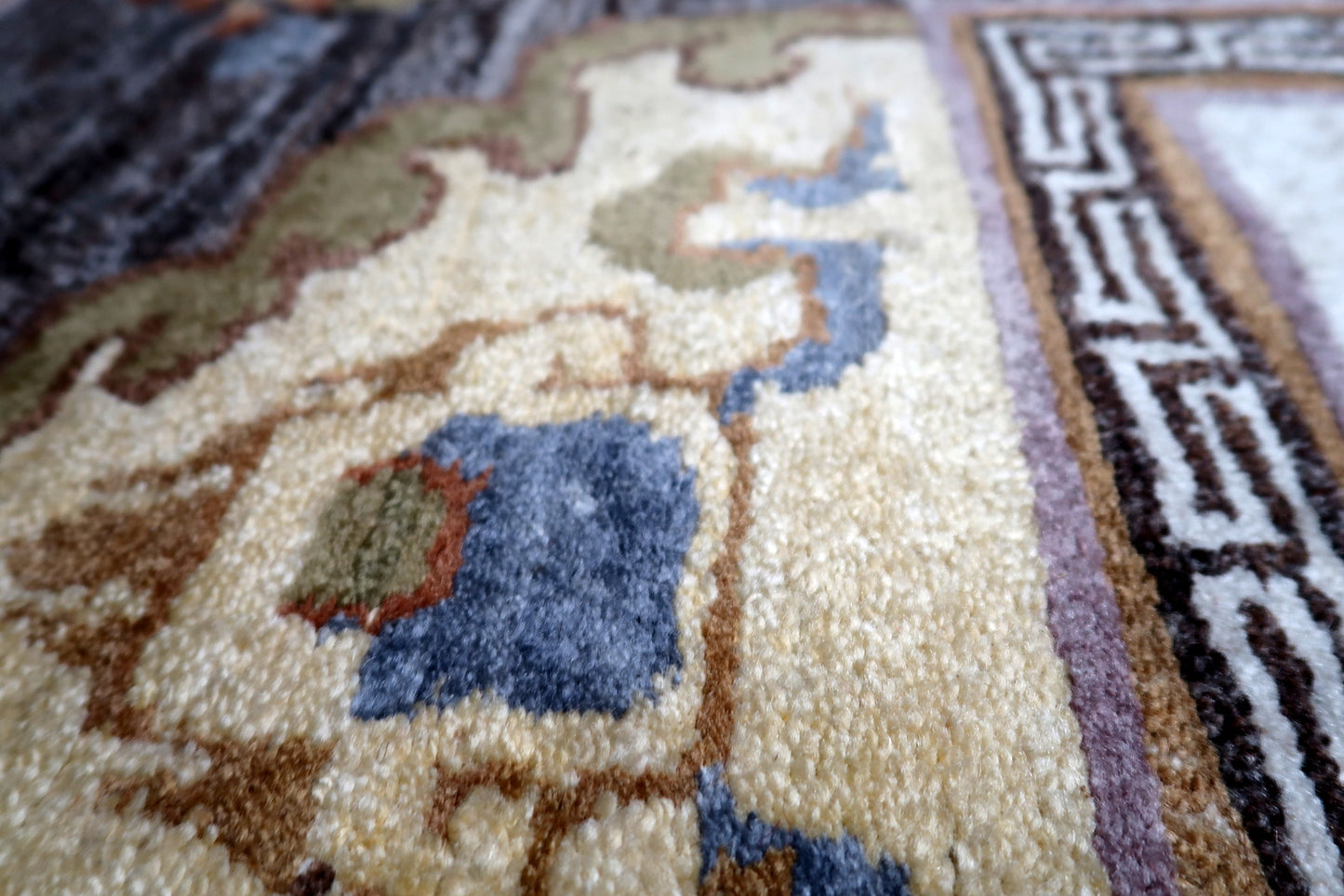 Detail of classic Greek key T-pattern border framing the central medallion on Tibetan carpet
