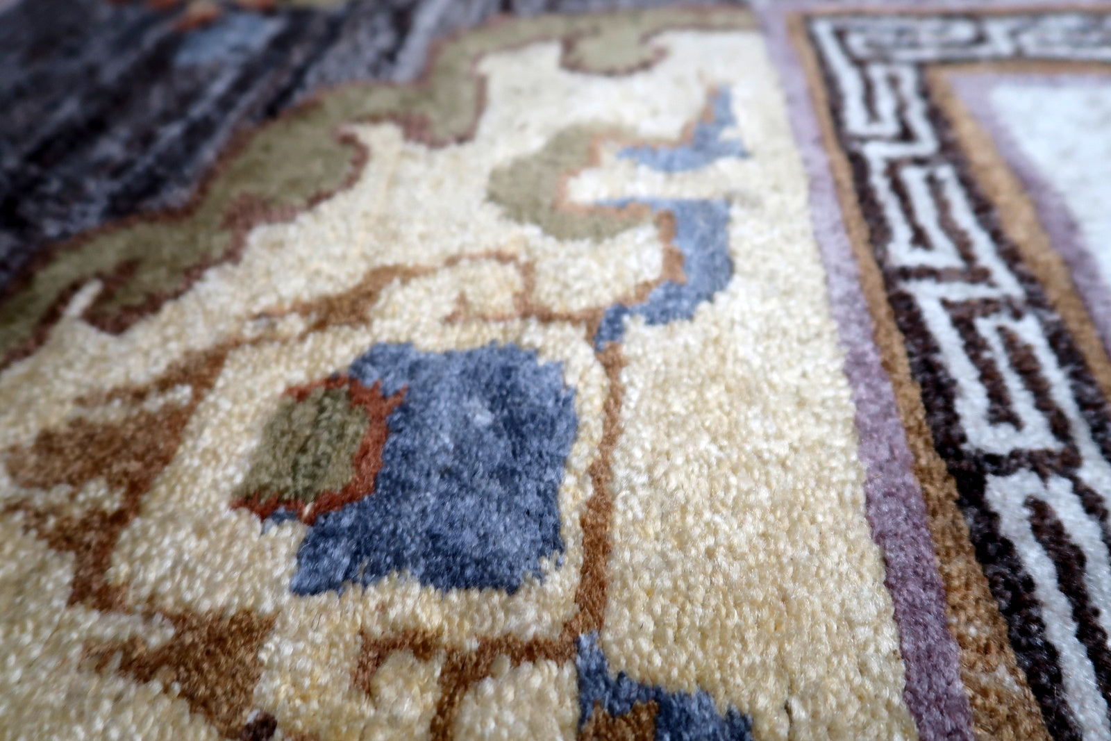 Detail of classic Greek key T-pattern border framing the central medallion on Tibetan carpet
