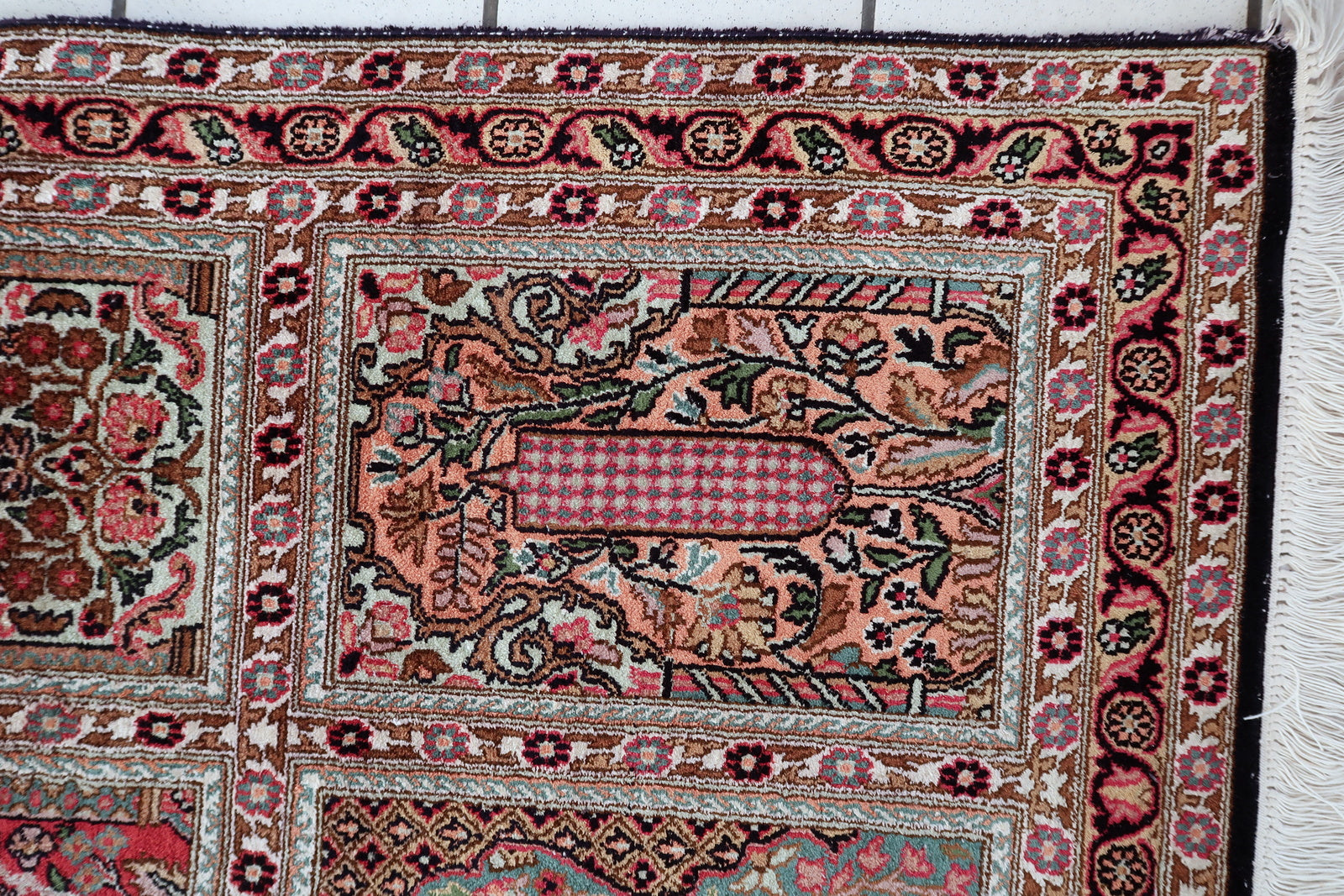 Qum silk rug corner detail, showcasing intricate border and aged patina