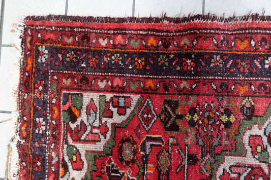 Close-up view of an authentic 1920s Persian Hamadan rug with intricate floral and geometric patterns in red, ivory, dark blue, and soft green.

