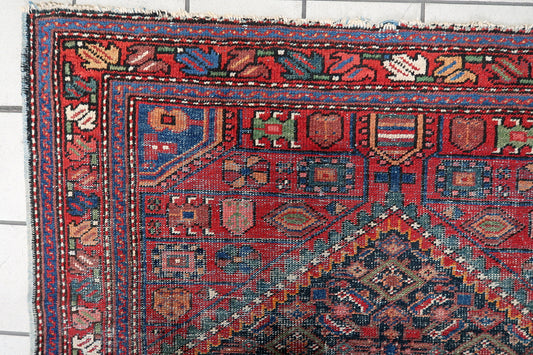 Close-up view of an authentic 1920s Persian Hamadan rug showing beautiful worn patina, low pile central field, and intricate geometric motifs on wool.

