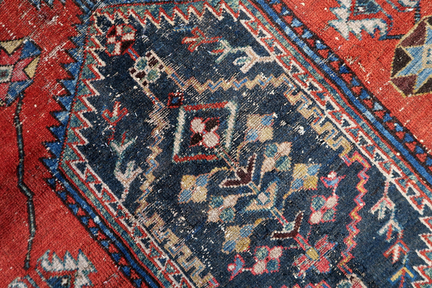 Authentic antique Persian rug with a warm, lived-in aesthetic, combining a red field, stylized ivory border motifs, and natural wear that enhances its old-world charm.

