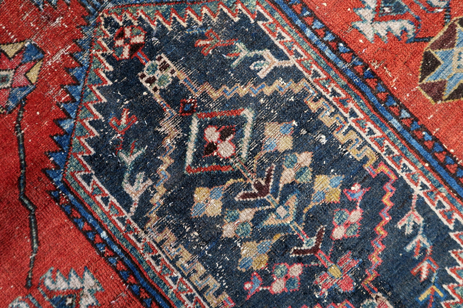 Authentic antique Persian rug with a warm, lived-in aesthetic, combining a red field, stylized ivory border motifs, and natural wear that enhances its old-world charm.

