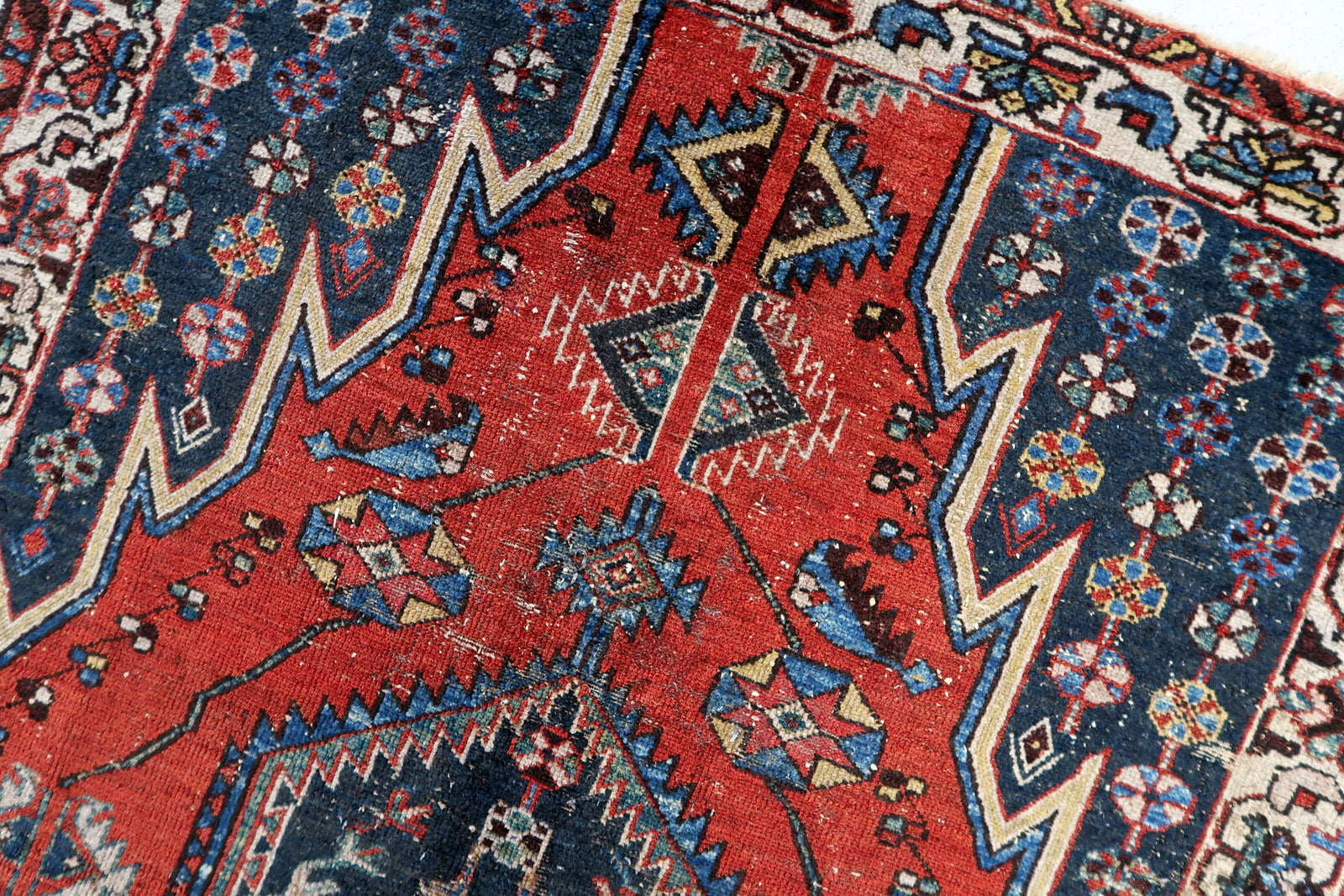 Vintage wool rug with a richly detailed pattern, featuring a dynamic interplay of red, navy, and ivory colors, and a softened, low-pile surface from decades of use.

