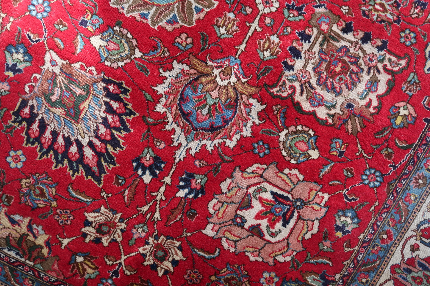 Full view of a room-size antique Tabriz rug with a classic and enduring color palette: deep crimson/lacquer red field, ivory/cream main border warmly toned with age, and teal/sky blue guard borders.

