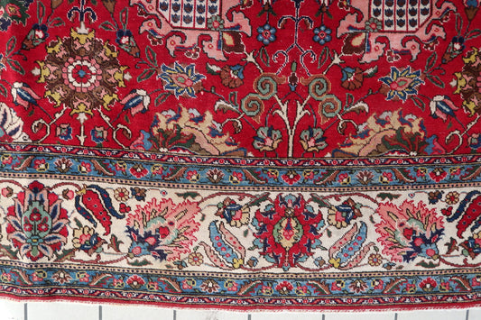 Close-up of a 1920s Persian Tabriz carpet showing the continuous interlocking vine system of the allover floral design: Shah Abbasi palmettes, open-faced lotus blossoms, Chinese-influenced cloud bands, serrated sickle leaves, and a pink vase motif on a warm crimson field.

