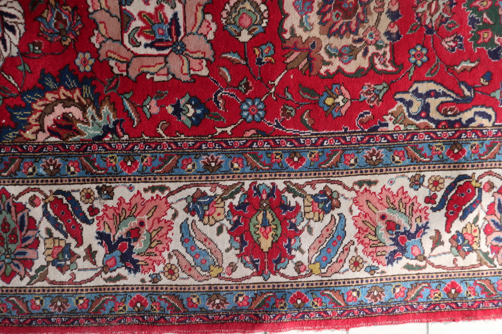 Close-up of the allover floral field pattern on a 1920s Persian Tabriz carpet, revealing Shah Abbasi palmettes at multiple scales, open-faced lotus blossoms in ivory and pink, cloud bands, and delicate flowering branches with blue daisies and pink rosebuds.

