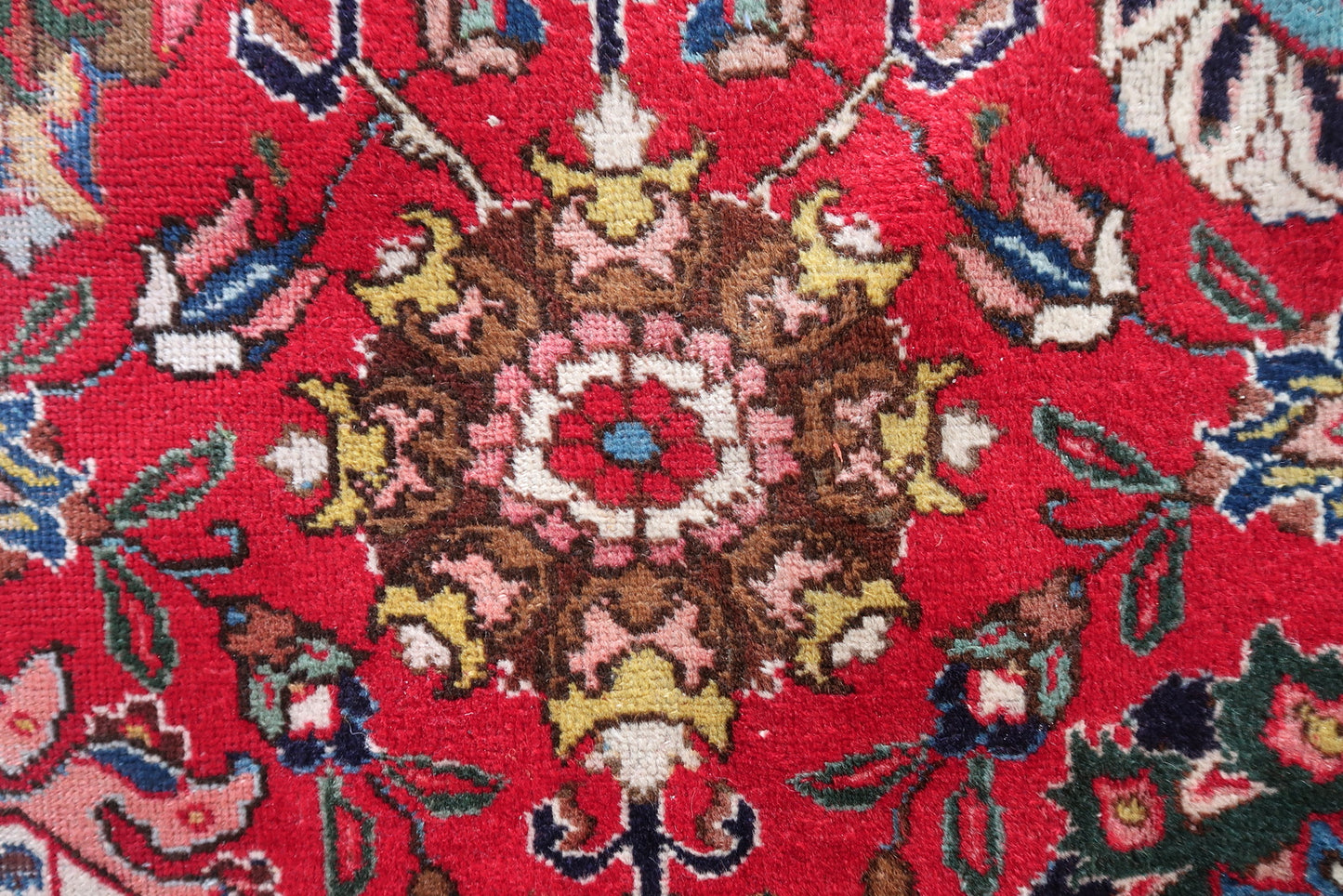 Detail of the deep crimson/lacquer red field on a vintage Persian Tabriz rug, showing the warm saturated color that shifts from scarlet to deep crimson as light changes, with navy and teal floral motifs.

