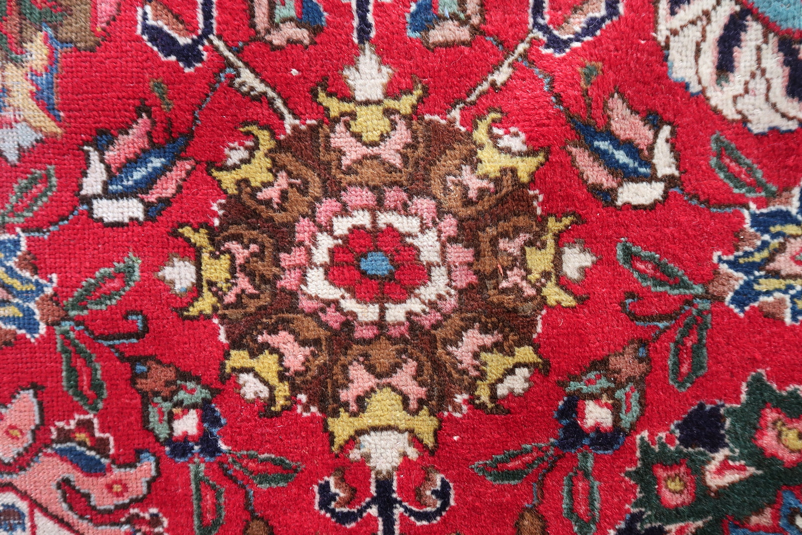 Detail of the deep crimson/lacquer red field on a vintage Persian Tabriz rug, showing the warm saturated color that shifts from scarlet to deep crimson as light changes, with navy and teal floral motifs.

