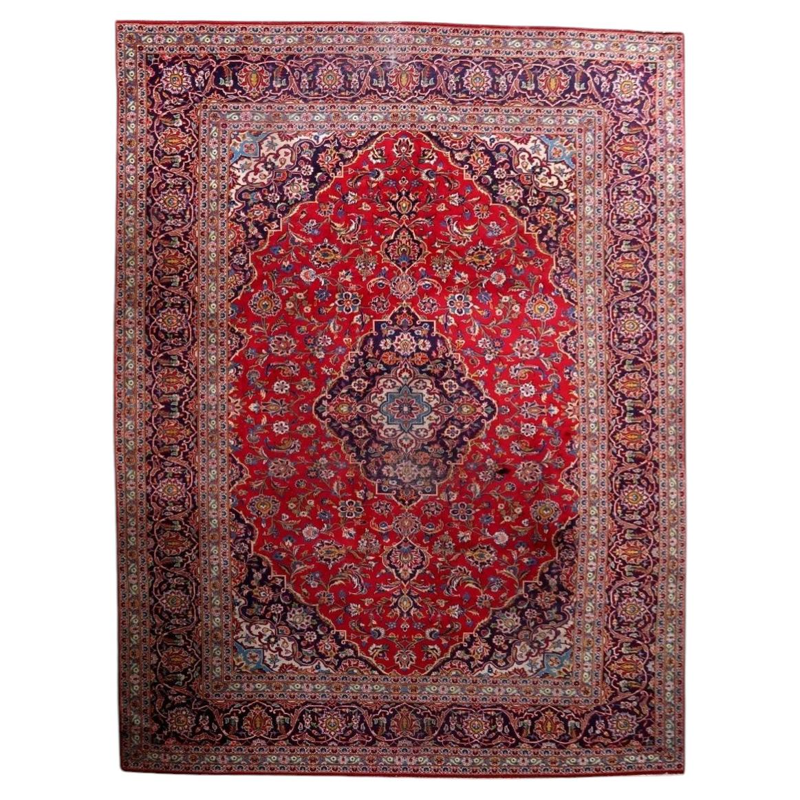 Full view of an antique Persian Kashan rug from the 1920s, featuring a large multi-lobed navy central medallion with an ivory center bearing a sky blue cross-star, surrounded by a deep crimson field with an allover floral scroll of dahlias, peonies, tulips, and palmettes, plus navy corner spandrels – a full room-size rug measuring 9.3 × 12.7 feet.

