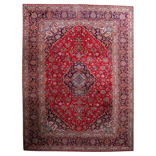 Full view of an antique Persian Kashan rug from the 1920s, featuring a large multi-lobed navy central medallion with an ivory center bearing a sky blue cross-star, surrounded by a deep crimson field with an allover floral scroll of dahlias, peonies, tulips, and palmettes, plus navy corner spandrels – a full room-size rug measuring 9.3 × 12.7 feet.


