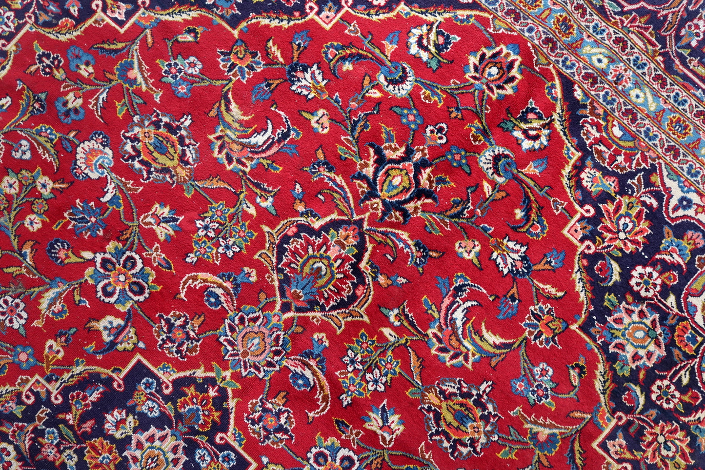 Full view of a room-size antique Kashan rug with a classic and commercially enduring color palette: deep crimson/lacquer red field, deep navy/indigo medallion and main border, vivid sky blue guard borders, and ivory arabesque scroll.

