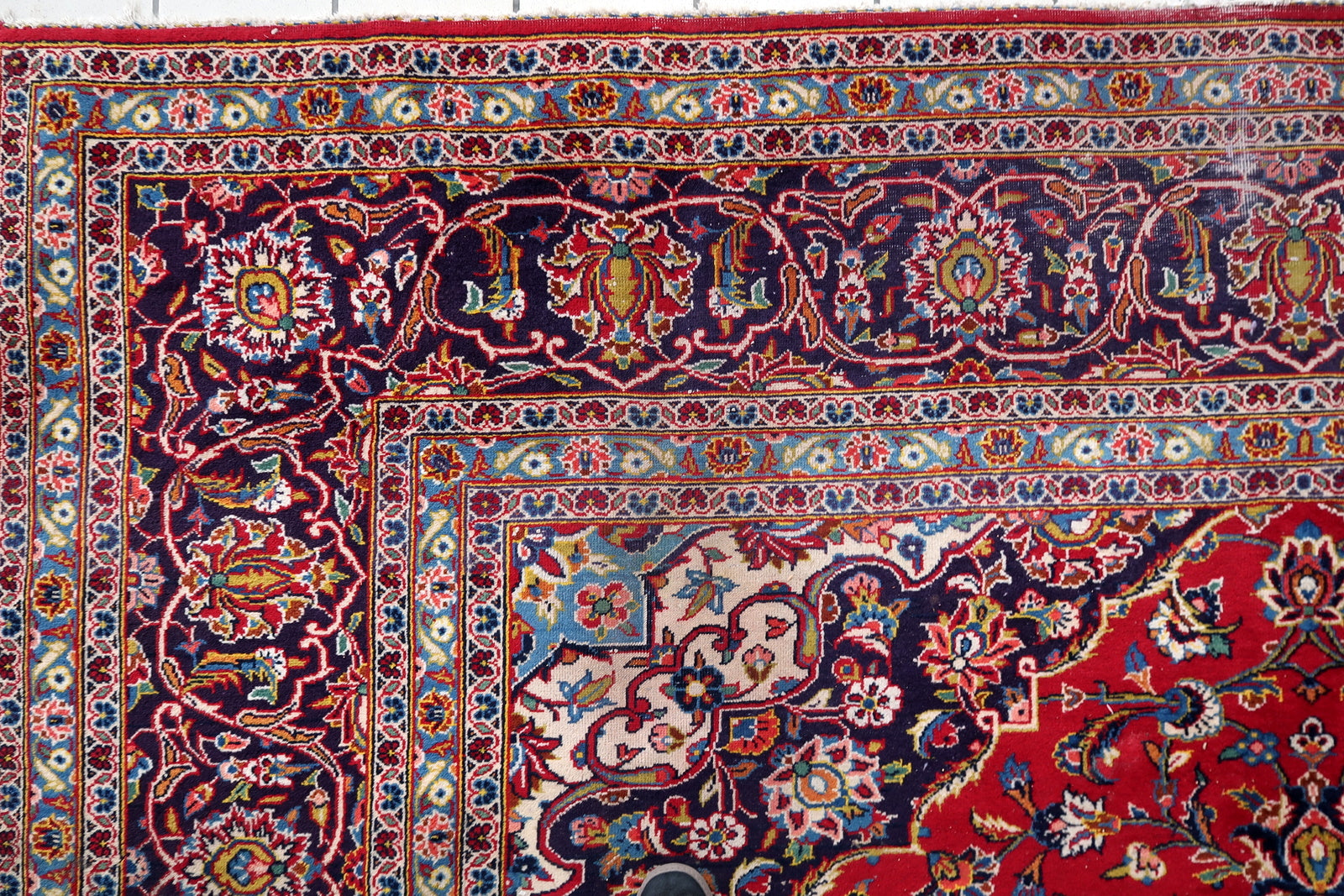 Detail of the wide navy main border on a 1920s Persian Kashan rug, showing large ivory arabesque forms with internal red and gold floral detail, navy palmettes outlined in ivory, and red rosette accents.


