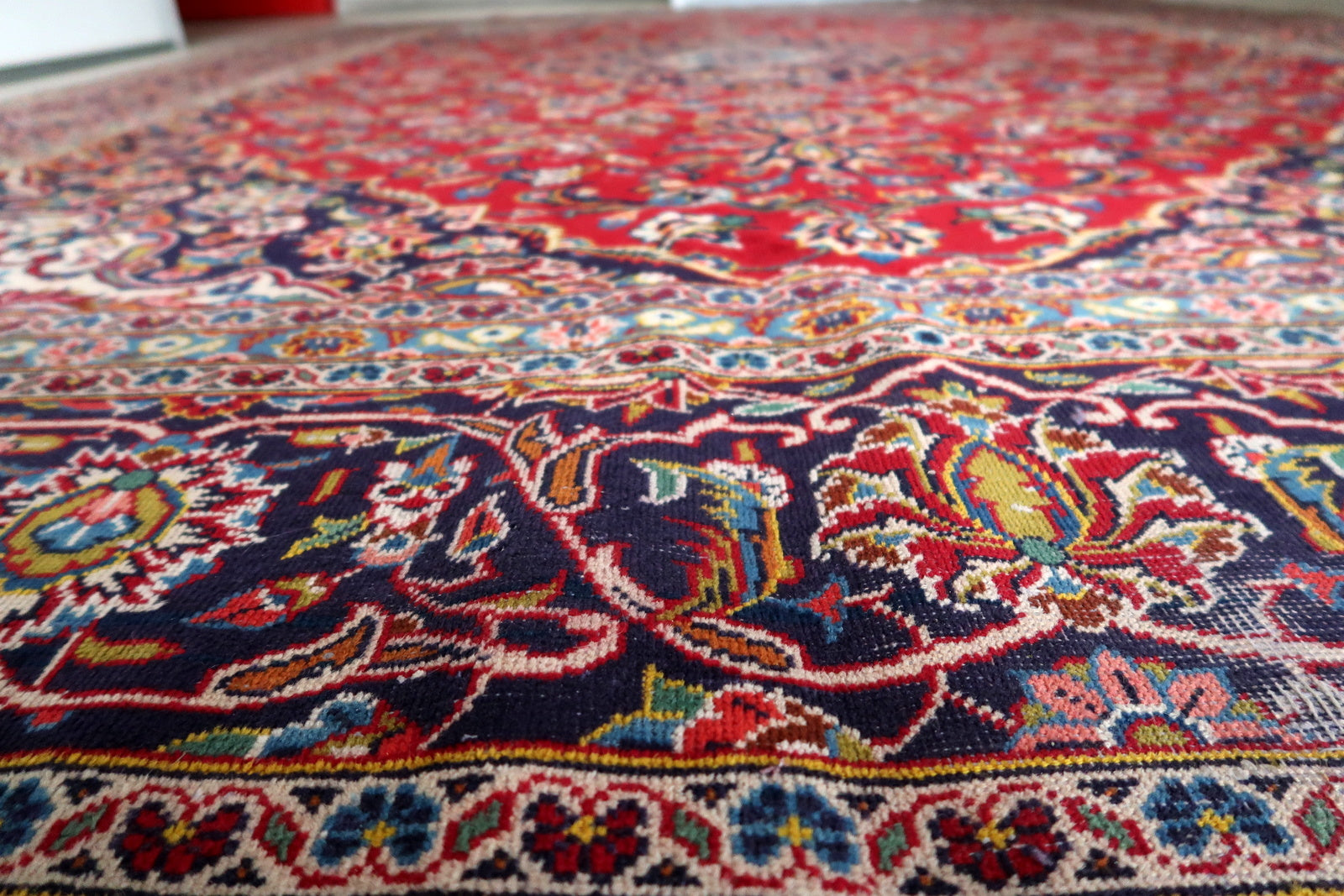 Detail of the sky blue inner guard border on a vintage Persian Kashan rug, showing vivid well-preserved blue with a continuous small floral rosette and vine scroll in red, ivory, and navy.

