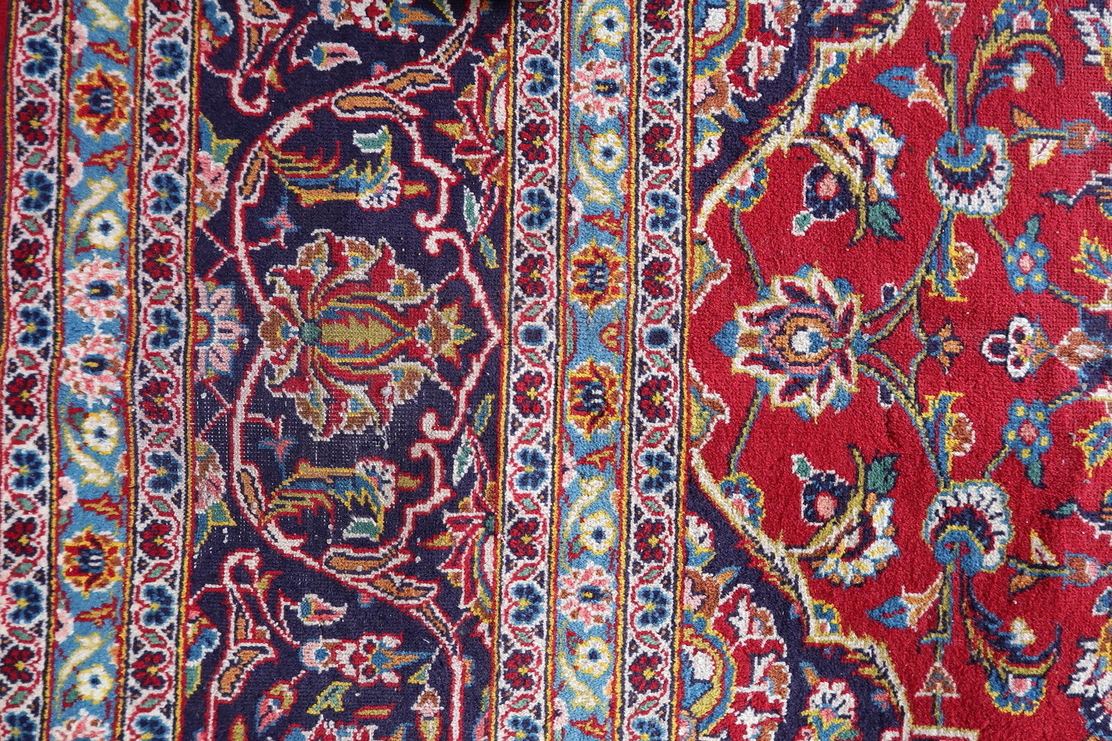 Detail of the border system on a vintage Persian Kashan rug, showing a deep navy main border with ivory arabesque scroll, vivid sky blue inner guard borders with floral rosette vine scroll, and ivory outer guard borders with small floral meander.

