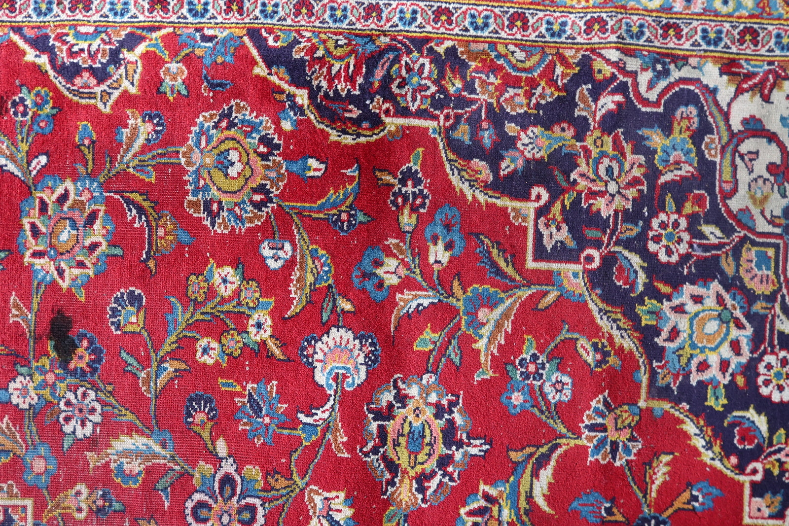 Close-up of the allover floral field pattern on a 1920s Persian Kashan carpet, revealing large multi-petalled dahlias and peonies in blue, ivory, pink, and gold, tulip forms, serrated olive leaves, and small rosette fillers on a deep crimson ground.

