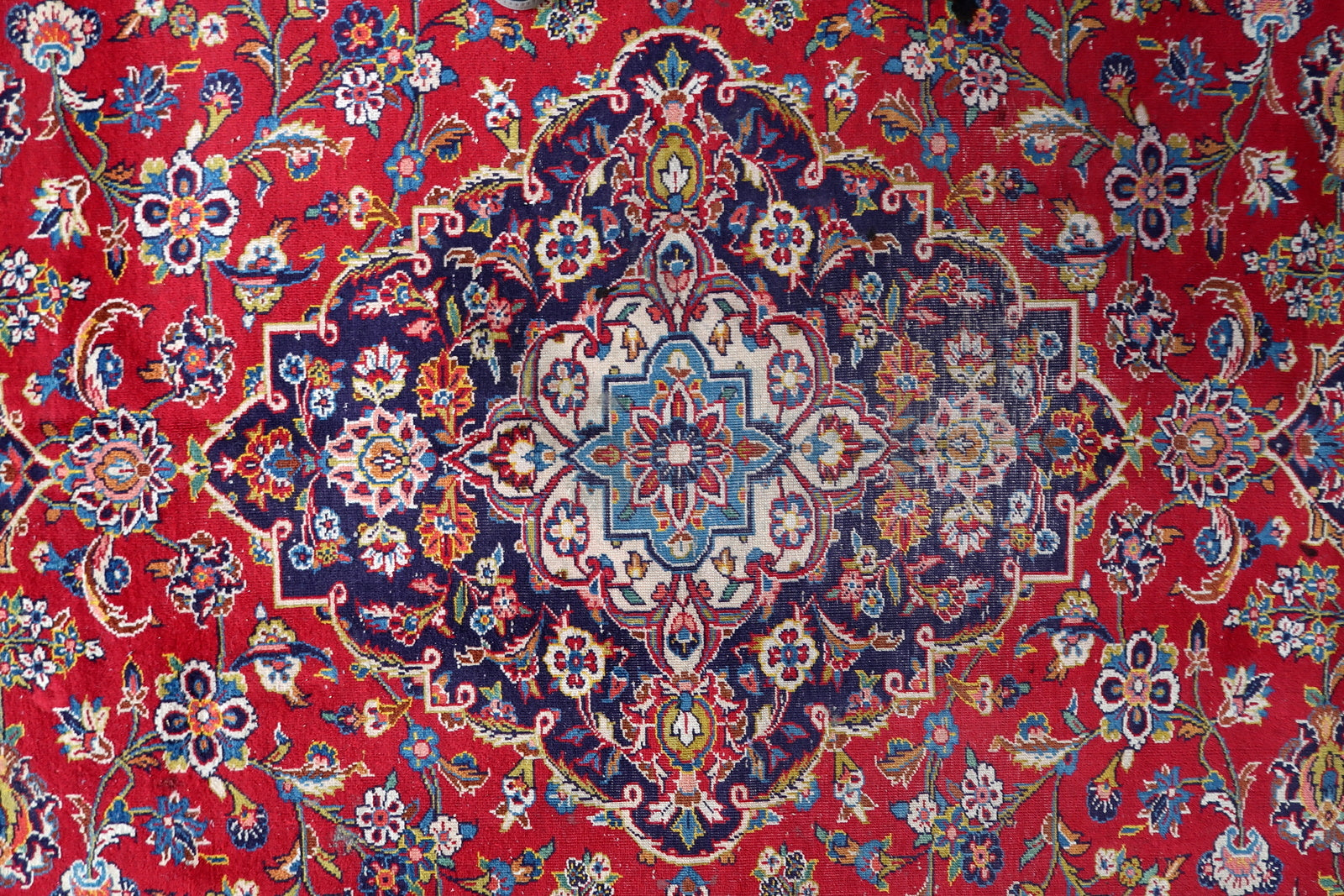 Detail of the deep navy corner spandrel on a vintage Persian Kashan rug, filled with the same dense floral vocabulary as the crimson field, creating the classic Kashan medallion-and-corner composition.

