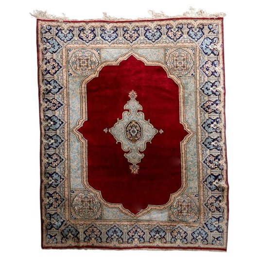 Full view of an antique Persian Kerman rug from the 1930s, featuring a vast open deep crimson/ruby red field with a single large cusped ivory medallion at center containing a delicate floral scroll in sky blue, pale pink, olive green, and gold, plus a teardrop pendant with pink floral ewer motif below – measuring 7.9 × 9.11 feet.


