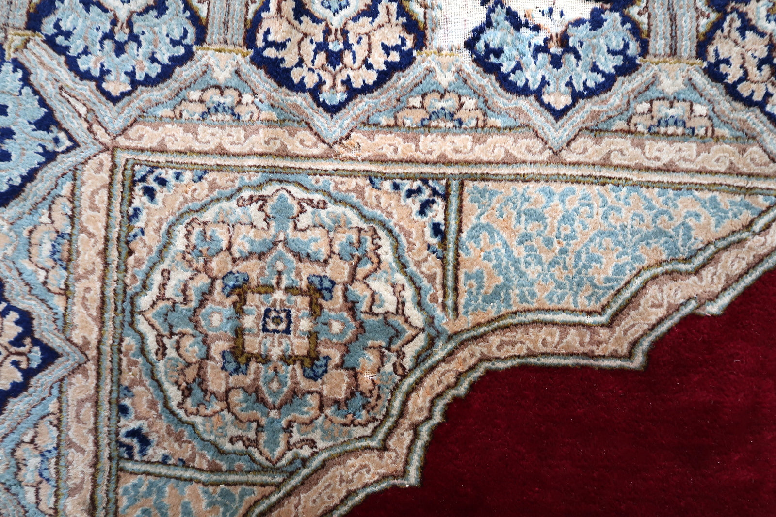 Full view of a room-size antique Kerman rug with elegant color palette: deep crimson/ruby red open field, large cusped ivory medallion with sky blue and pale pink floral scroll, deep navy arcade border with ivory arch forms.

