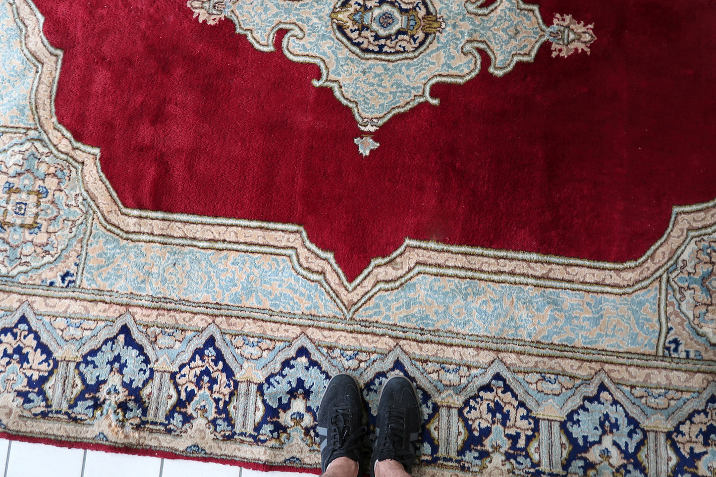 Detail of the deep navy outer main border on a 1930s Persian Kerman rug, showing large ivory pointed arch forms with sky blue floral fills on the navy ground, repeating in a bold graphic rhythm around all four sides.

