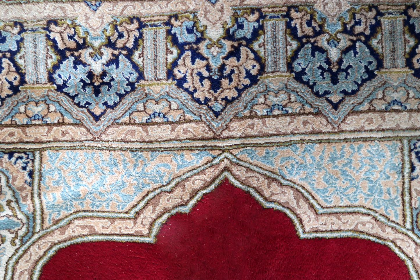 Detail of the border system on a vintage Persian Kerman rug, showing a wide ivory/pale blue inner sub-border with light floral scroll, multiple narrow guard strips in pink, navy, and ivory, and a deep navy outer main border with ivory arcade/arch forms and sky blue floral fills – inspired by Islamic muqarnas and mihrab architecture.


