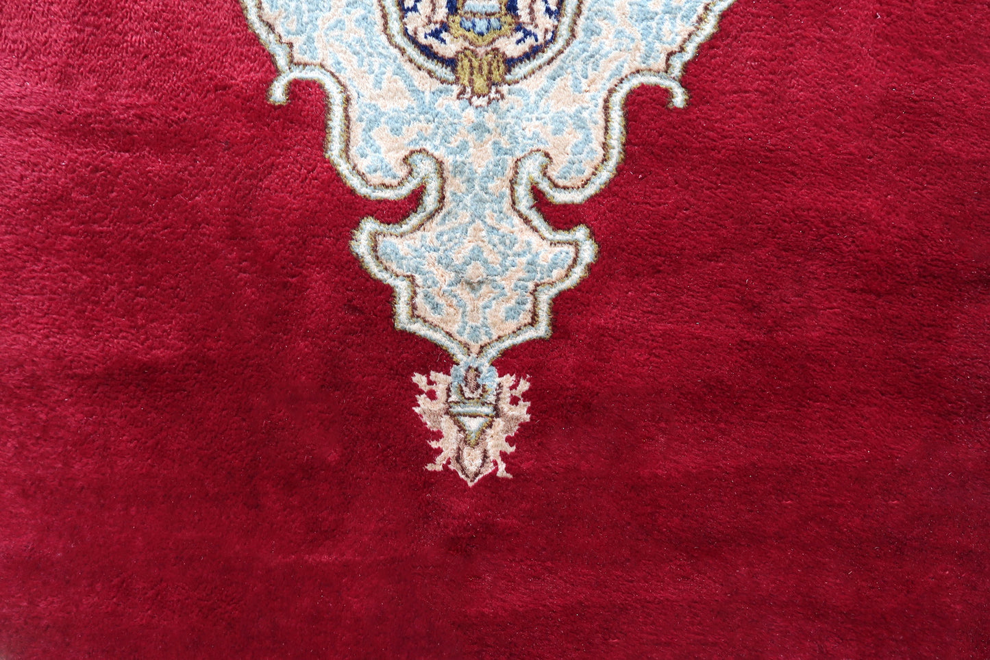 Detail of the teardrop pendant on a vintage Persian Kerman open field medallion rug, showing the ivory and pale blue form tapering to a point and tipped with a small pink floral ewer motif – one of the most elegant single motifs in the Kerman repertoire.

