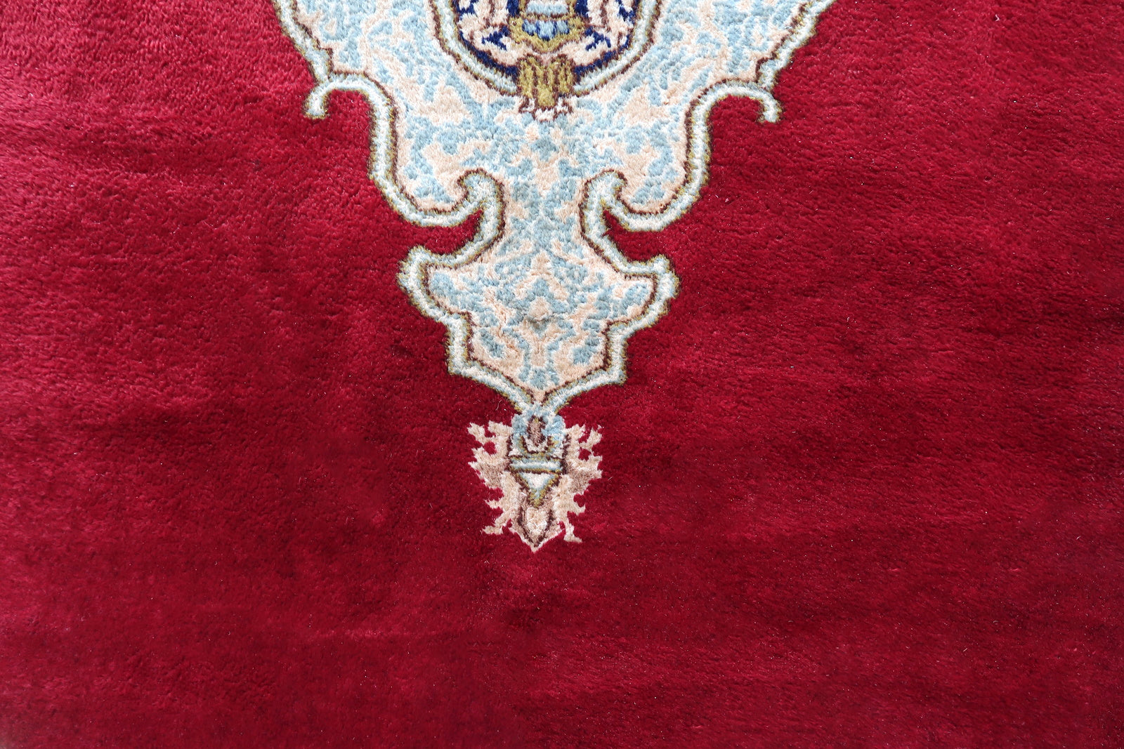 Detail of the teardrop pendant on a vintage Persian Kerman open field medallion rug, showing the ivory and pale blue form tapering to a point and tipped with a small pink floral ewer motif – one of the most elegant single motifs in the Kerman repertoire.

